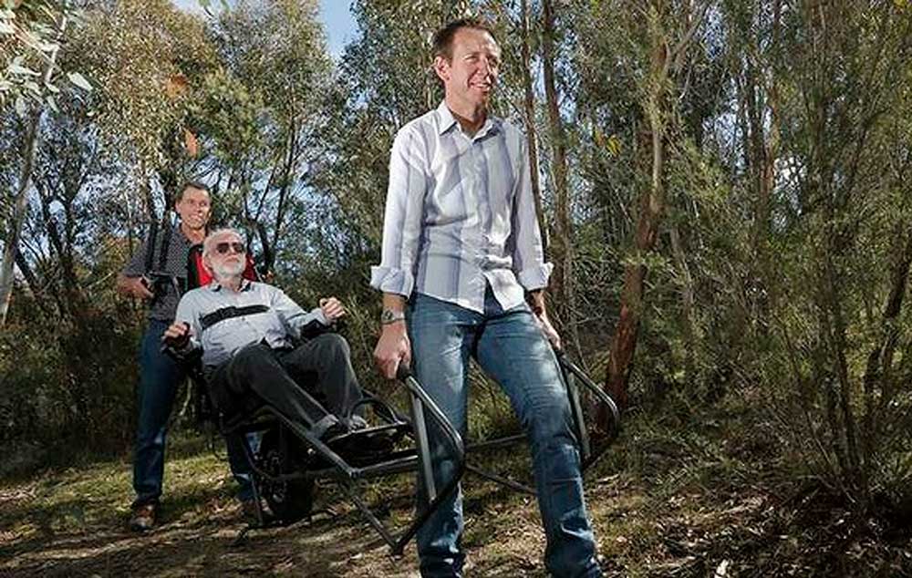 National Parks Association president Rod Griffiths(centre) gets some help testing out a new wheelchair from Peter Clarke from Lyneham and Shane Rattenbury MLA at the Tidbinbilla Nature Reserve