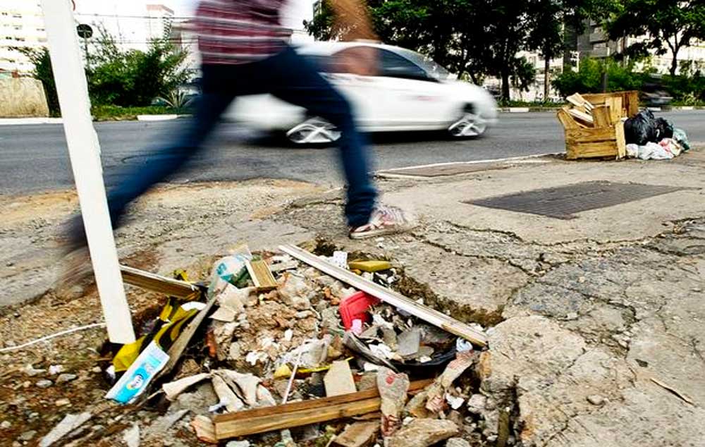 Pedestre salta por cima de um buraco na calçada da avenida Engenheiro Luís Carlos Berrini, em São Paulo