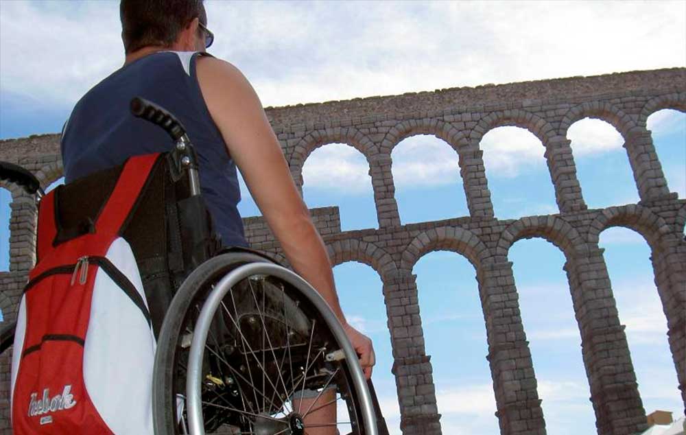 Turista en silla de ruedas mirando el acueducto romano de Segovia