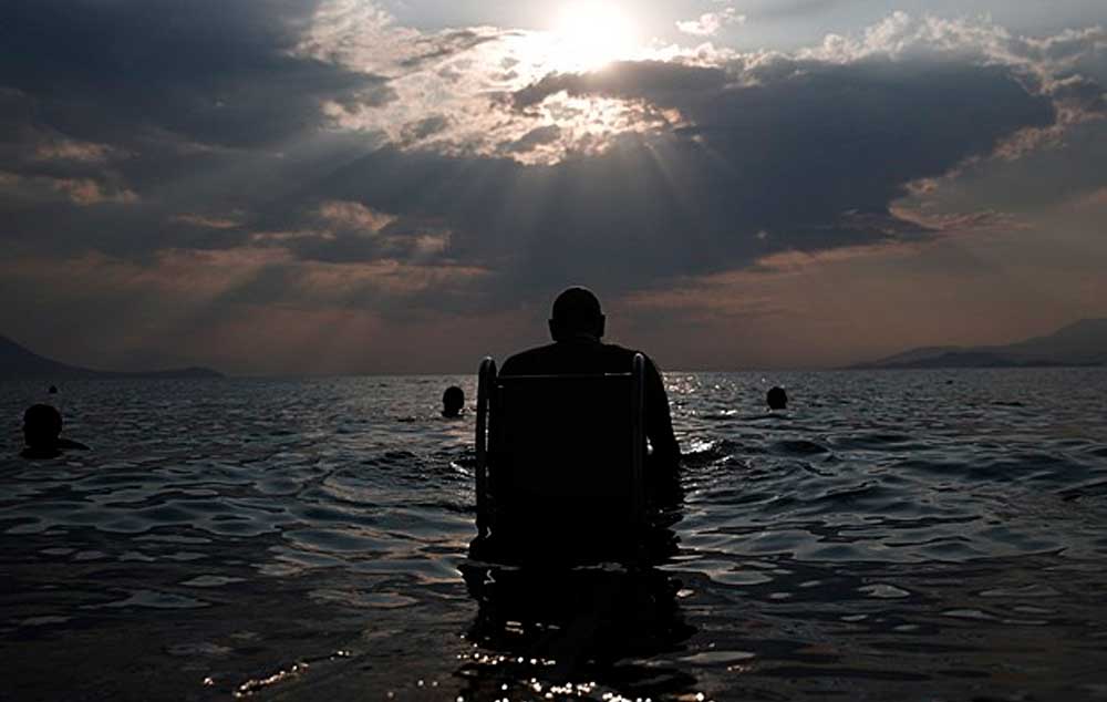 Lefteris Theofilou, de 52 anos, que sofre de paraplegia, entra no mar com a ajuda do Seatrac, dispositivo movido a energia solar na praia de Alepochori, no oeste de Atenas