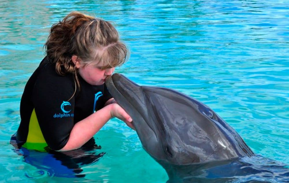 Eliza Sprague, with rett syndrome, kisses a dolphin at Atlantis in the Bahamas. Her mother has never let that stop the family from traveling extensively.