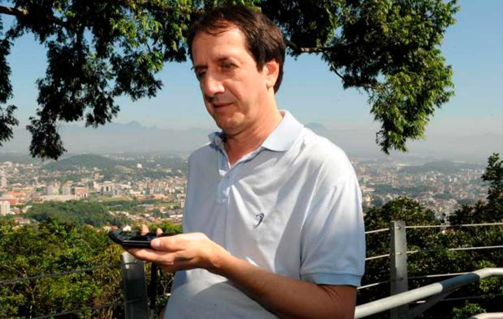 O professor Osmar Pavesi, que é deficiente visual, usa um telefone celular para ouvir a audiodescrição