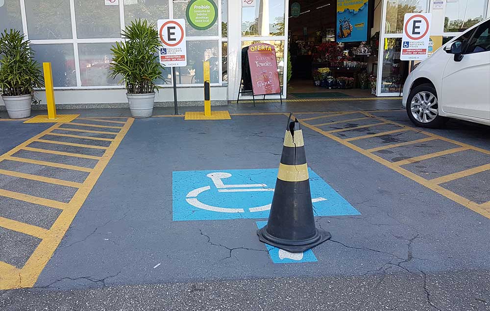 Cone de bloqueio para vaga reservada. foto mostra uma vaga reservada de estacionamento para pessoas com deficiência, com demarcações pintadas no chão e placa de informação, e um cone de trânsito colocado no meio da vaga.